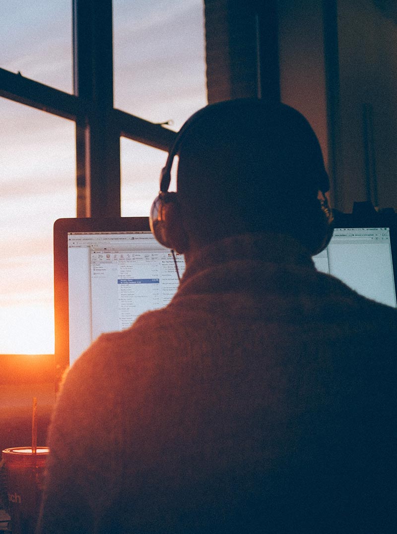 uomo con cuffie davanti ad un monitor visto da dietro accanto a finestra con vista