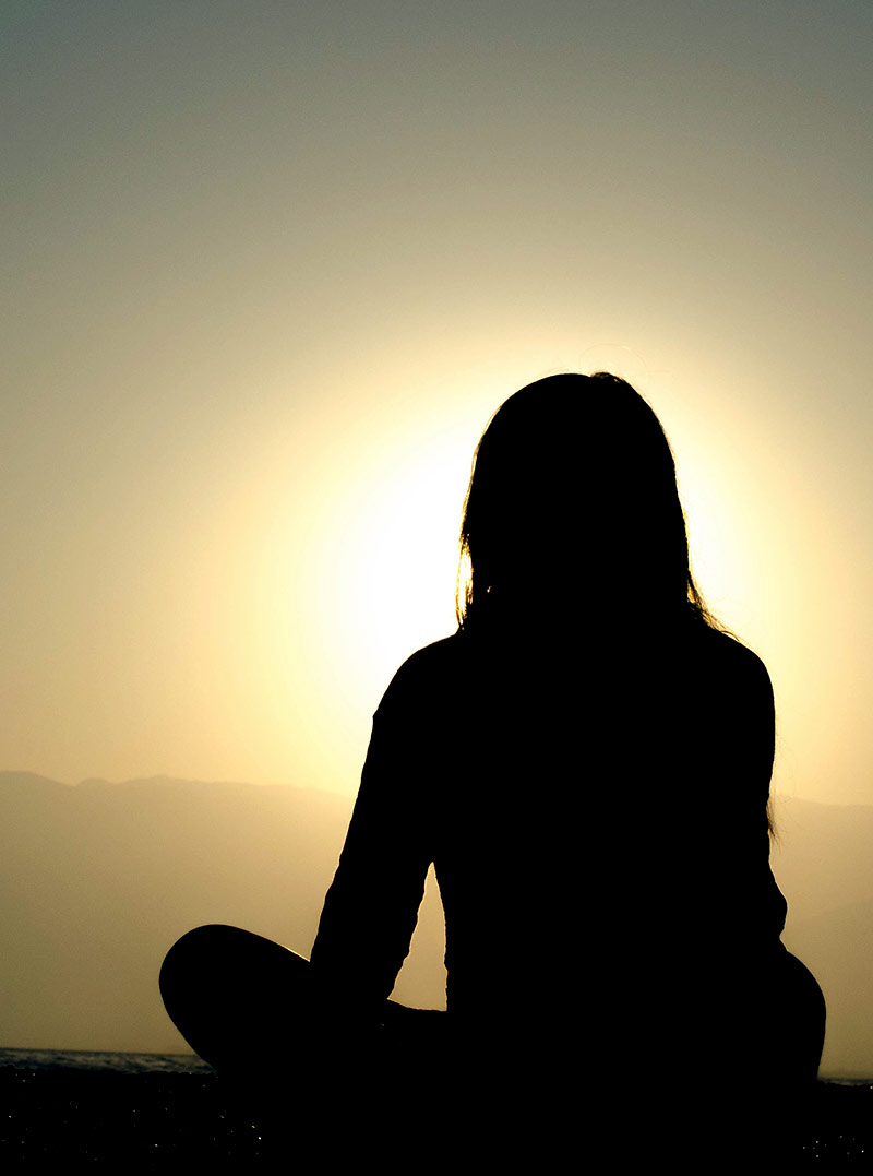 donna seduta a gambe incrociate davanti ad una vista sui monti al tramonto