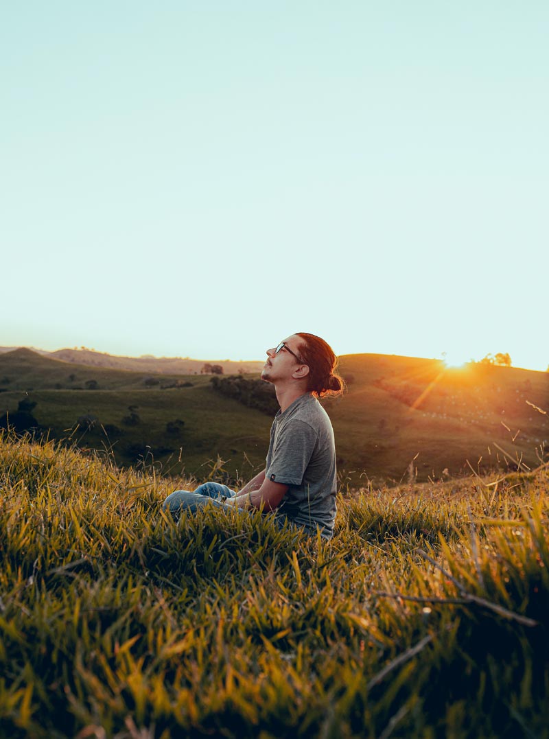 ragazzo con occhiali e codino medita al tramonto in un campo